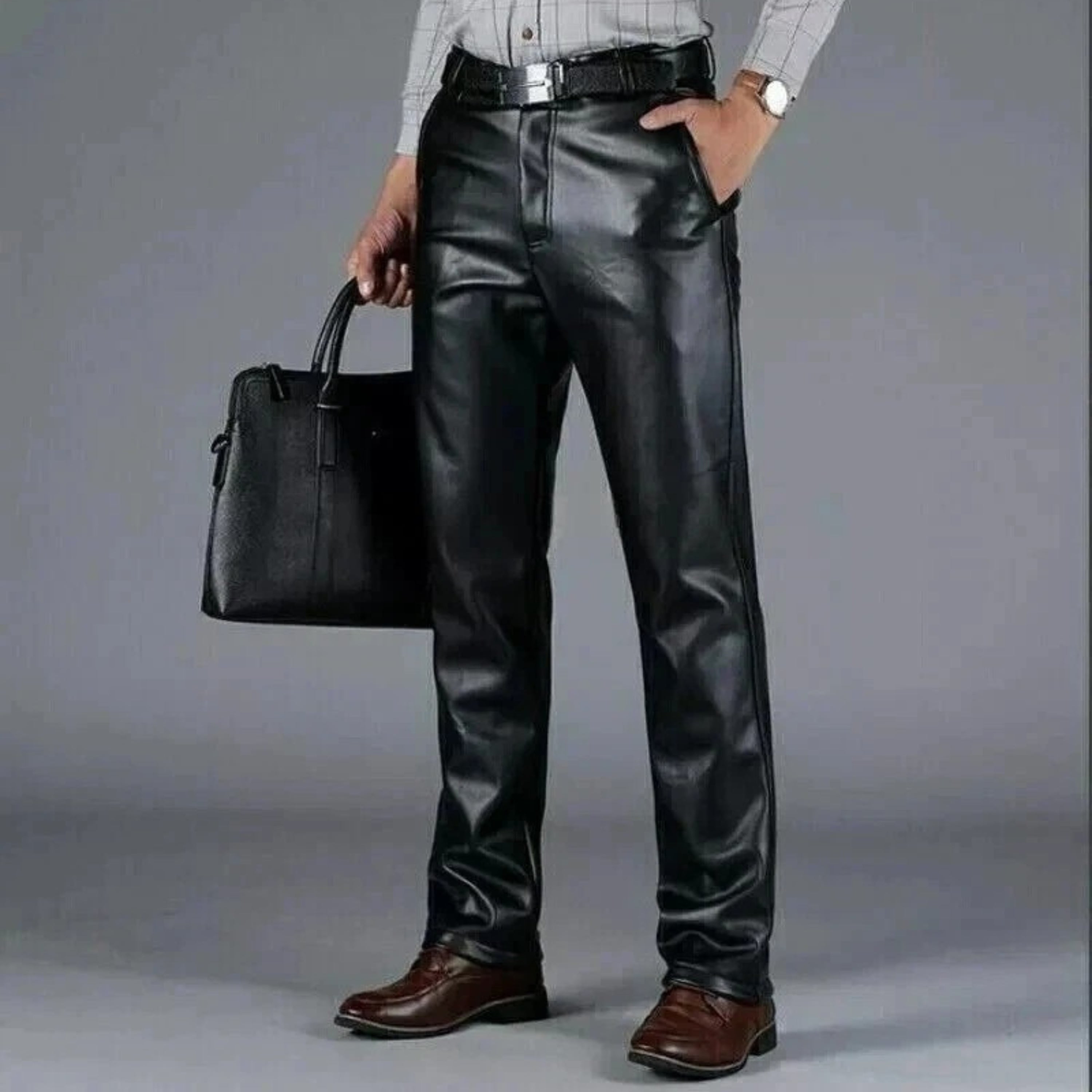 Person wearing black leather pants holding a black bag on a gray background