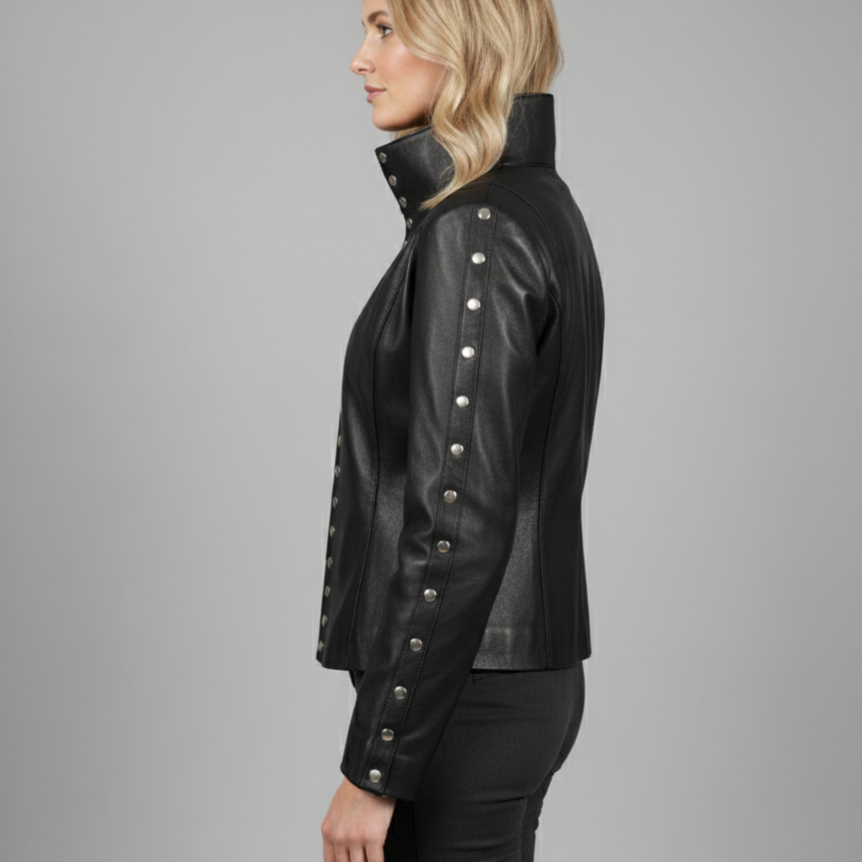 Woman wearing a black leather jacket with silver buttons on a gray background